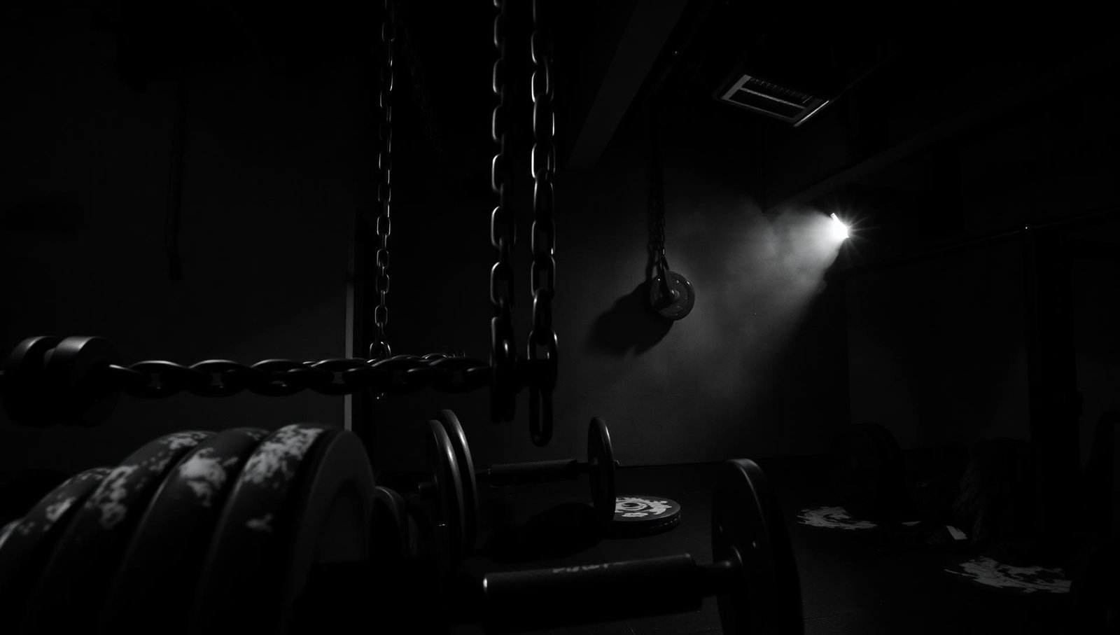 Interior oscuro del gimnasio Mutant Gym con pesas y cadenas
